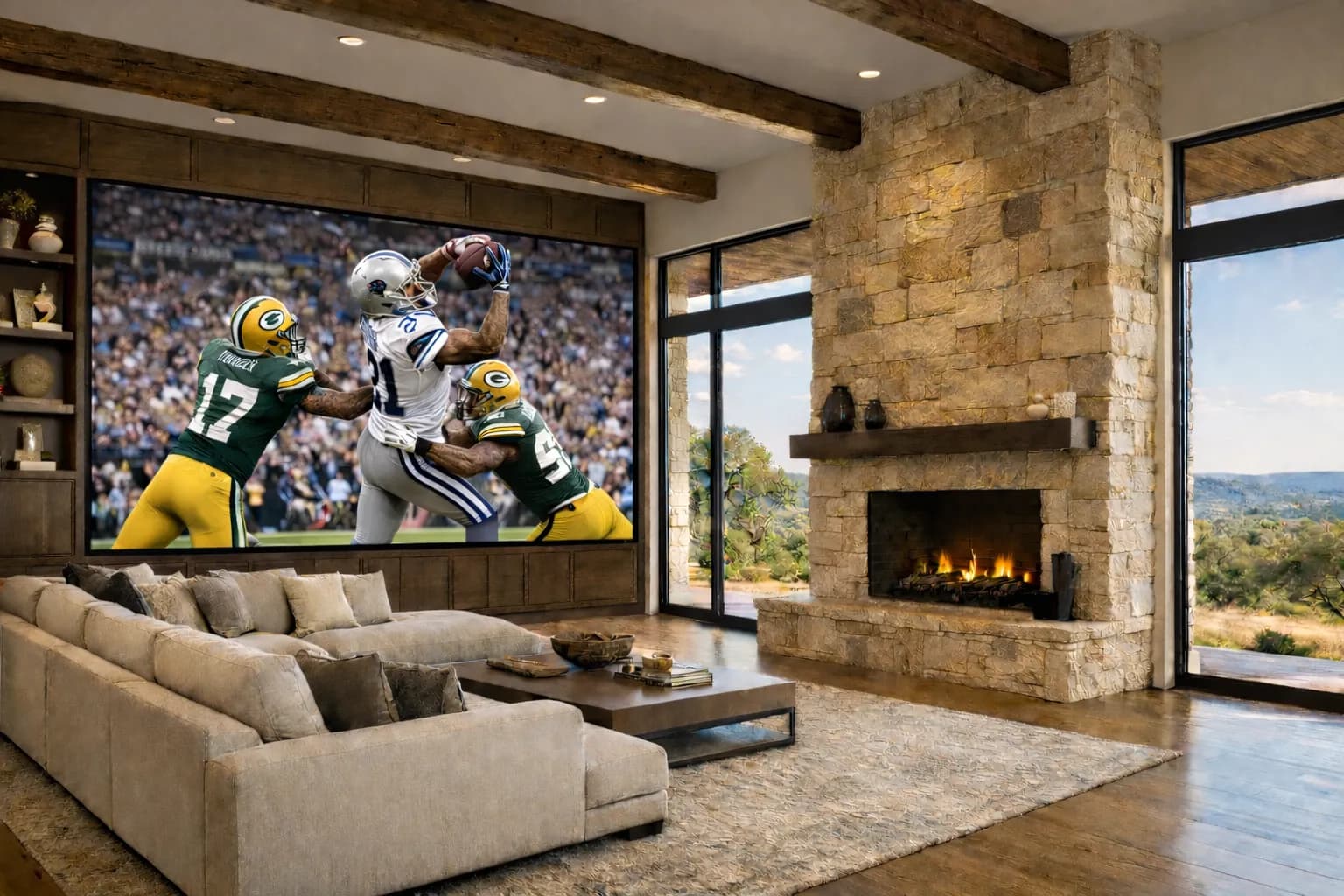 Living room with a stone fireplace, timber beams, and a wall-size LED Video Wall showing a football game, with windows looking out over the hills